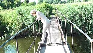 A sexy milf walks naked on a hanging bridge over a nudist river beach.