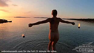 A pretty woman performs nude fire dancing on the beach at sunset.
