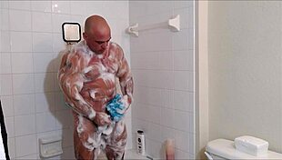 muscular guy soaps oiled body in shower