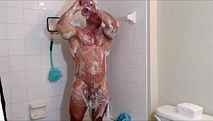 muscular guy soaps oiled body in shower